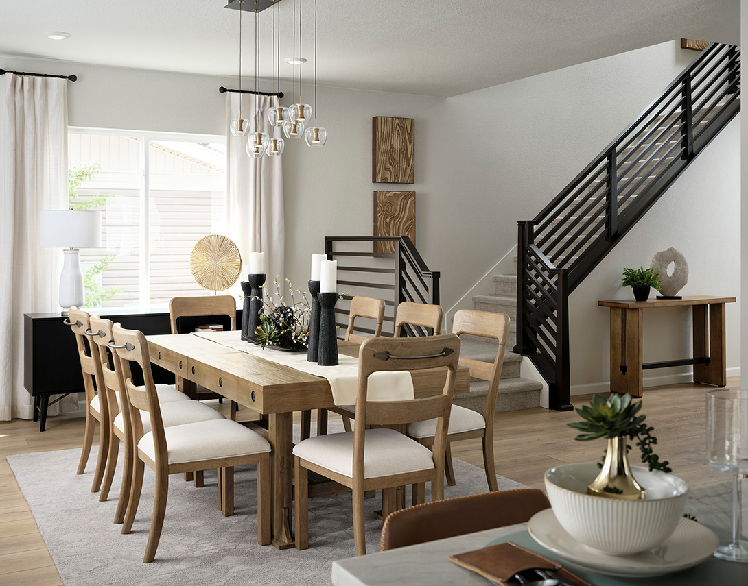 A dining room with a wood dining room table and chairs and a horizontal railing leading upstairs in the background.