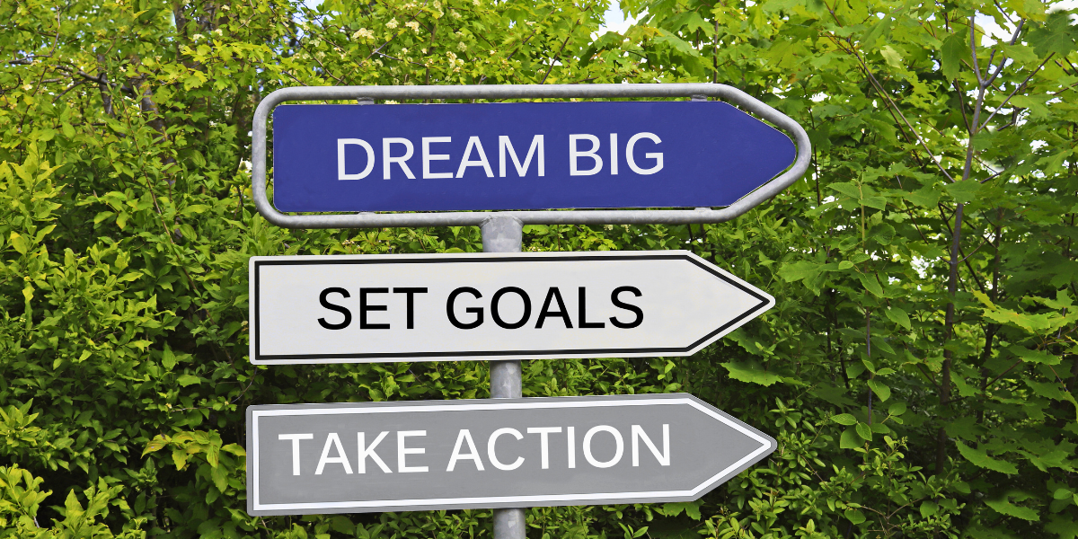 Street sign showing three arrows that say "Dream Big", "Set Goals", and "Take Action"