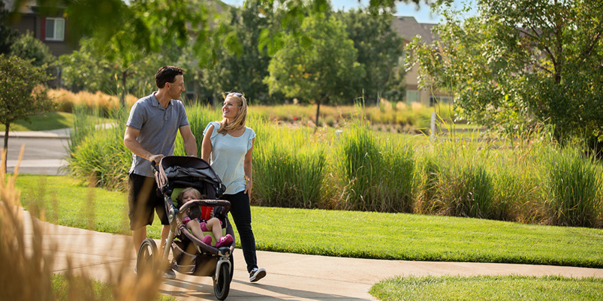 Couple walking a stroller  along a grassy trail in the sunlight