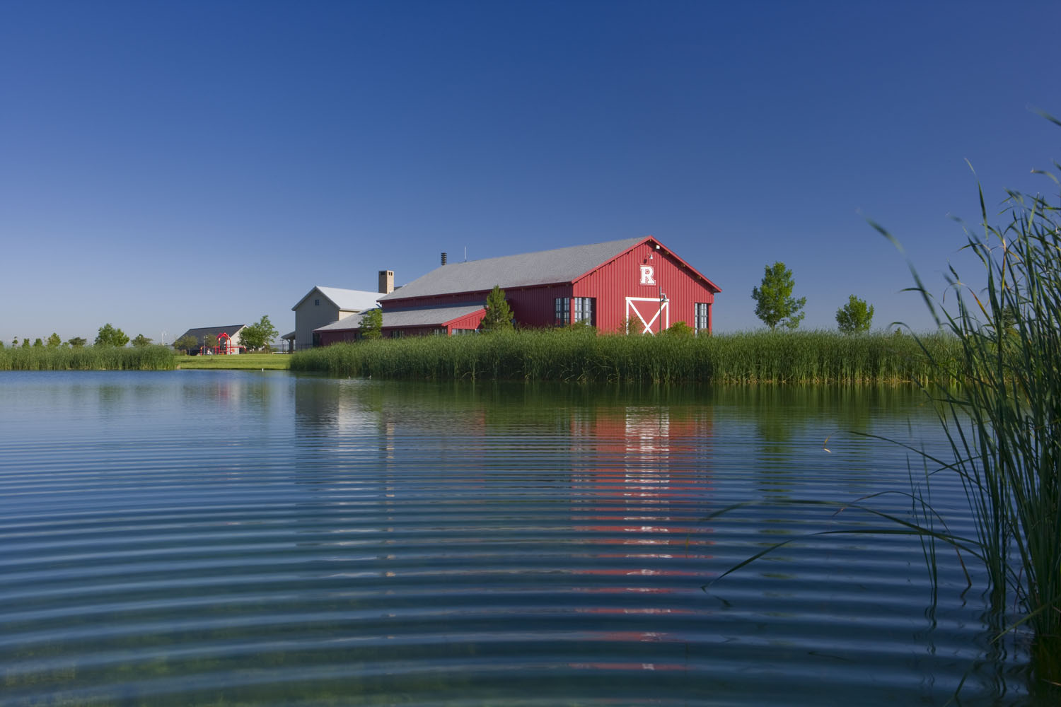 A red barn that is Reunion's rec center shown on a grassy edge next to a large lake. 