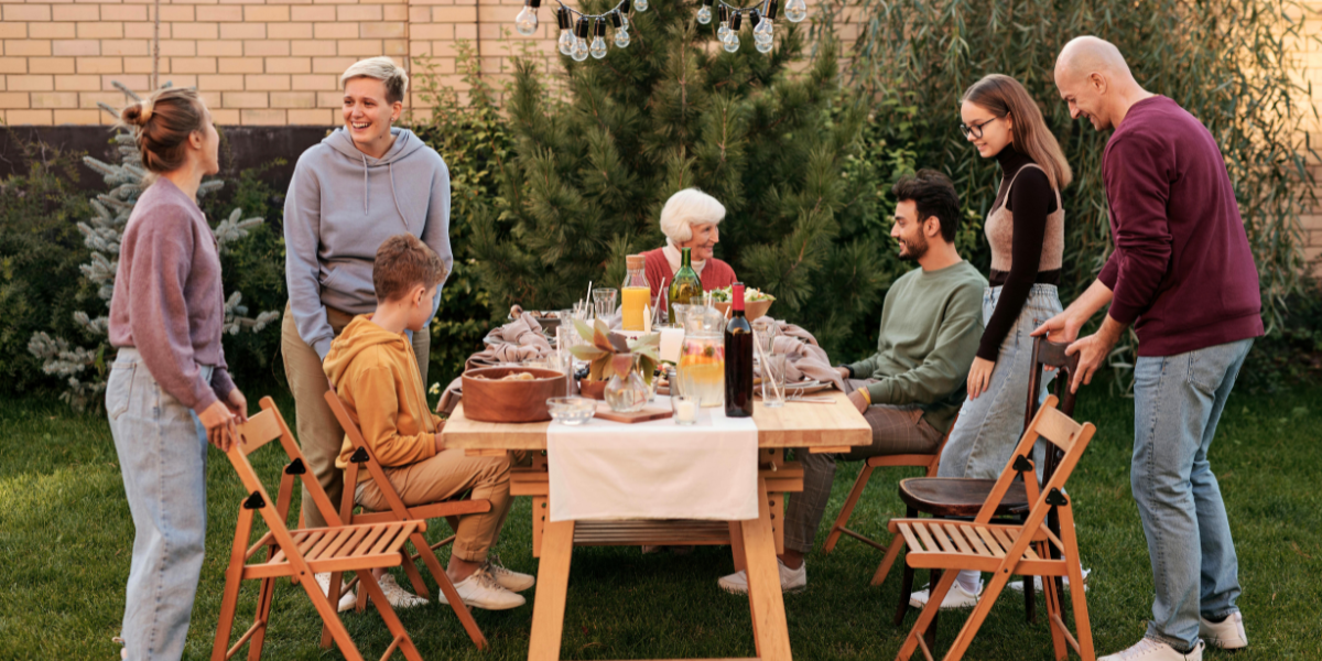 Family sits at a nicely decorated table in their backyard to enjoy a meal together. 