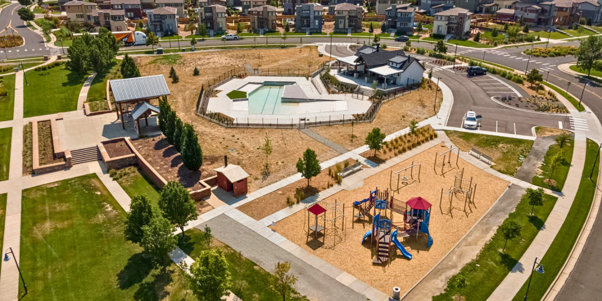 Aerial view of large outdoor swimming pool and neighboring park with a playground.