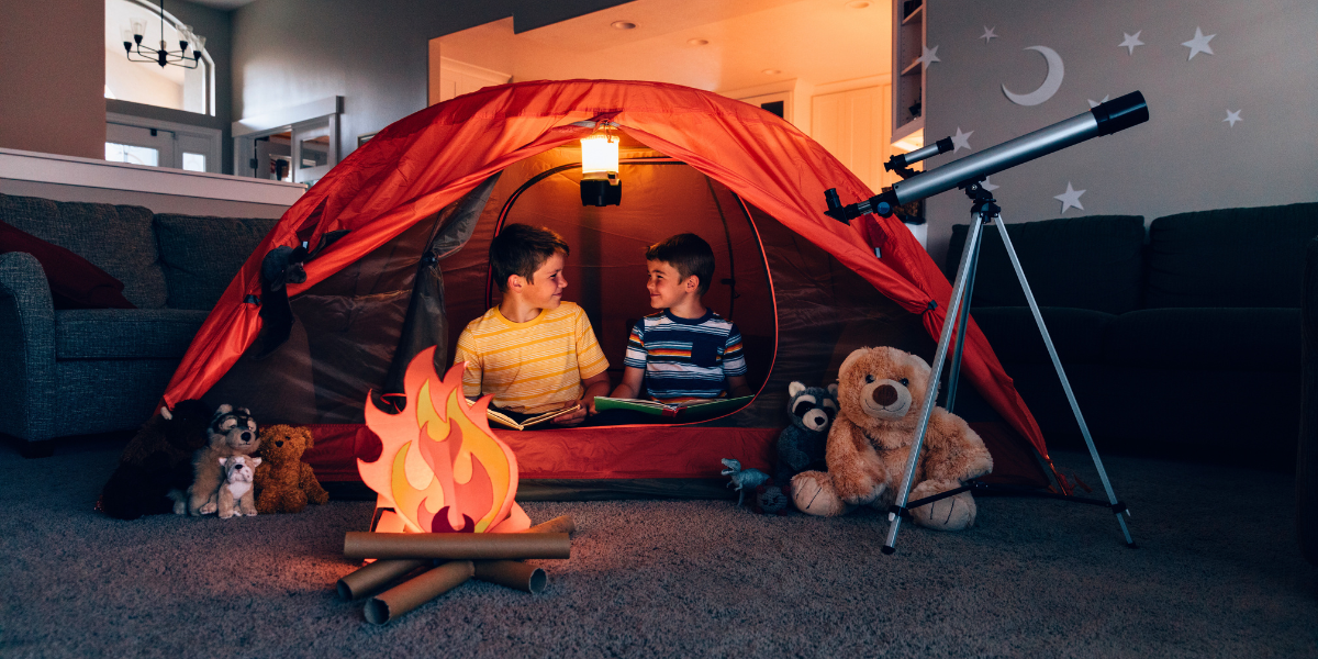 Children inside a tent indoors, with a little campsite setup inside their room.