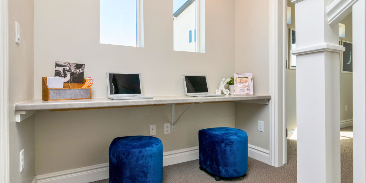 Smart hub setup with a shelf on the wall with computers, outlets, and smart devices and ottomans to sit on. 